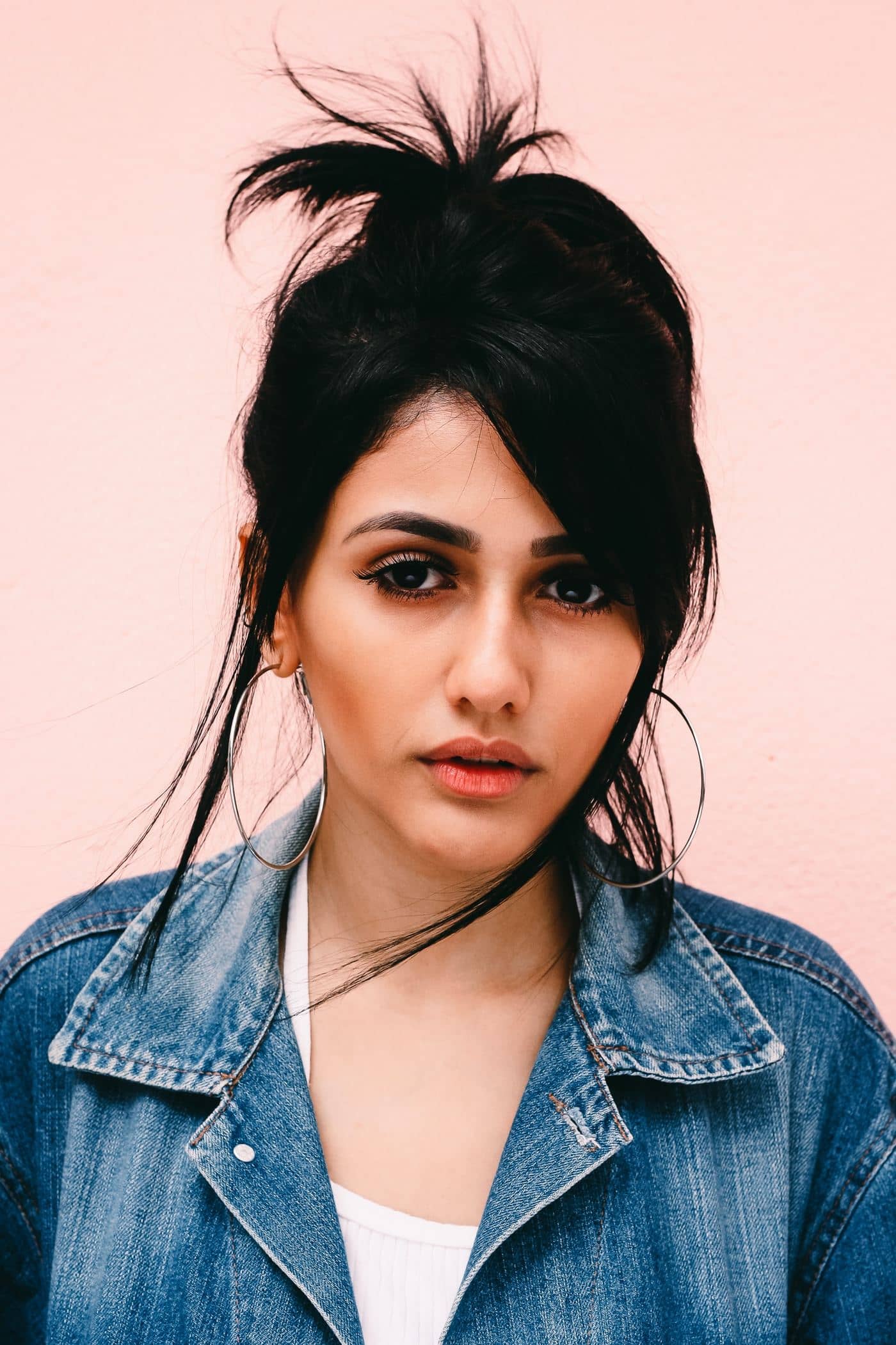 Portrait of a woman in a denim jacket with hoop earrings and messy bun.